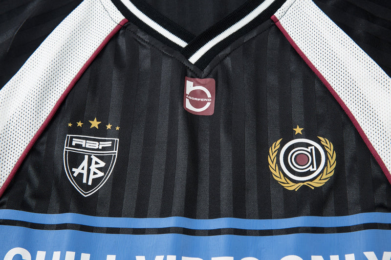 Front chest close-up of black football jersey with crest patches and CHILL VIBES ONLY print