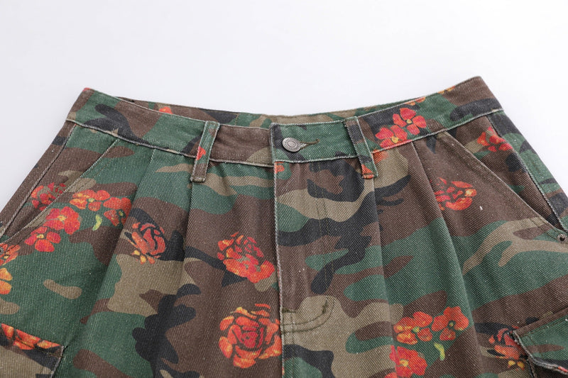 Close-up of floral camo shorts front waist with pleats, button closure, and belt loops