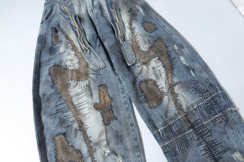Front view of distressed patchwork wide-leg denim pants with hanging waistband straps