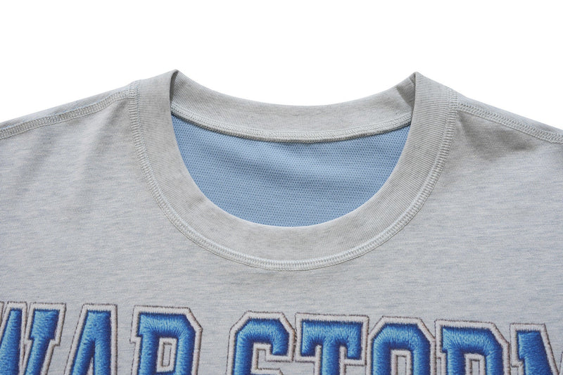 Close-up of a light gray varsity graphic tee with blue mesh lining and bold blue collegiate lettering