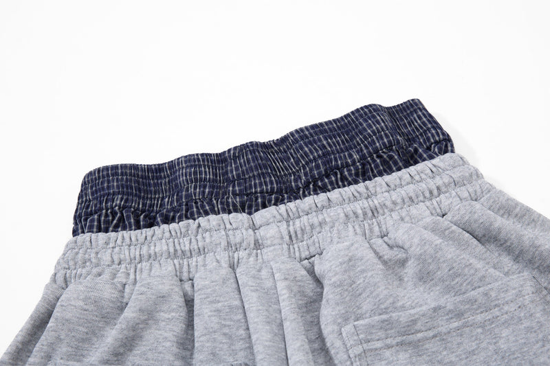 Close-up of light gray shorts with navy plaid waistband and white side stripes