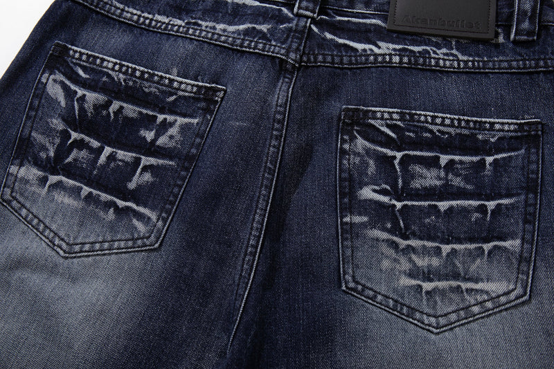 Back pocket close-up on deep indigo jeans showing cracked-wash fading and topstitching