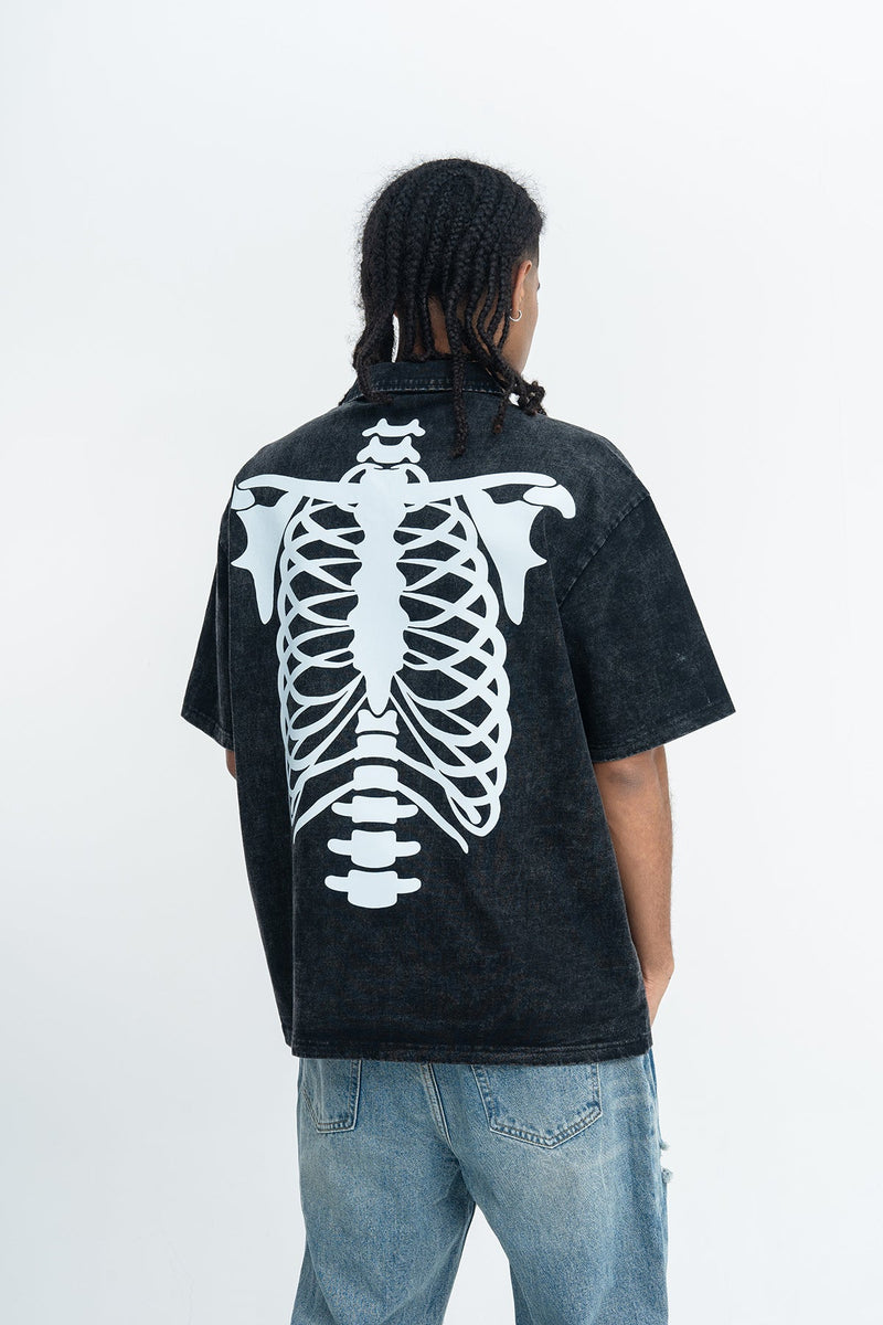 Black washed polo shirt with oversized white spine skeleton graphic on the back, shown on a model with jeans