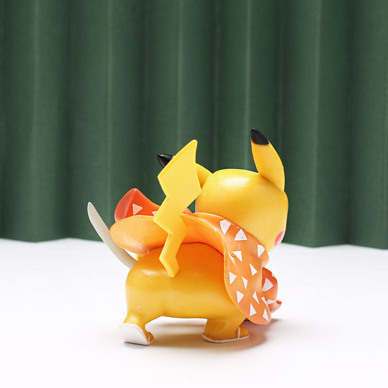 A Pikachu figurine from the Demon Slayer collection is dressed in a Halloween-themed orange and black costume featuring triangular patterns and bat wings, positioned with its back to the camera against green curtains.