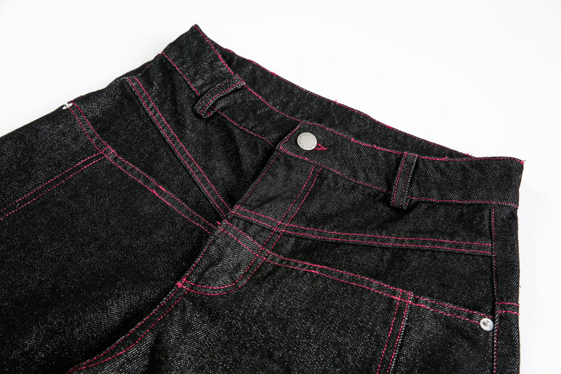 Close-up of black denim waistband with red stitching and silver button
