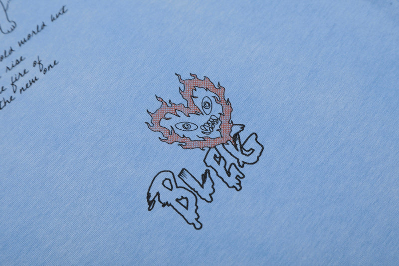 Light blue graphic tee with a small flaming cartoon face and handwritten-style sketch print on soft cotton fabric