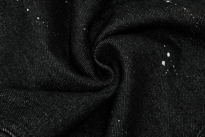 Black denim fabric folded with visible weave texture and white paint splatter