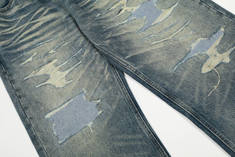 Close-up of distressed ripped patches on faded blue jeans legs