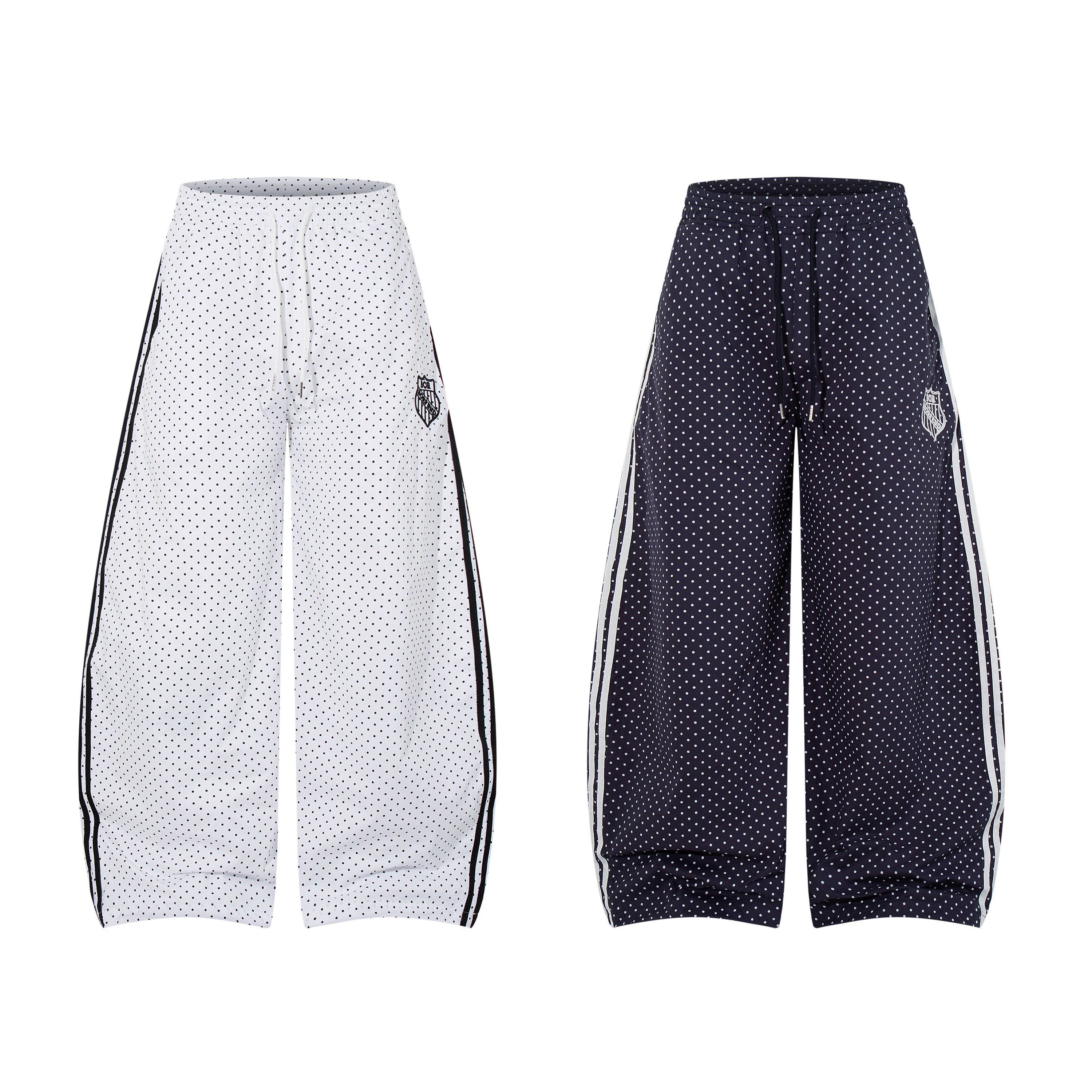 White polka dot wide-leg track pants with contrast black side stripes and embroidered crest badge on white background