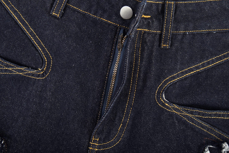 Close-up of the front fly on dark jeans showing zipper, button, and stitched pocket detail