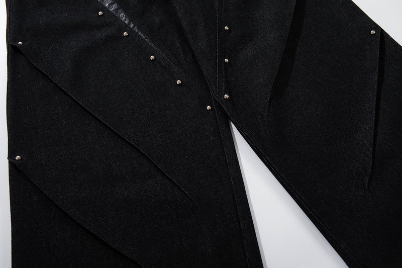 Close-up of black denim legs with diagonal panel seams and rivets