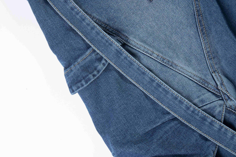 Close-up of blue denim side seam with diagonal cargo pocket panel