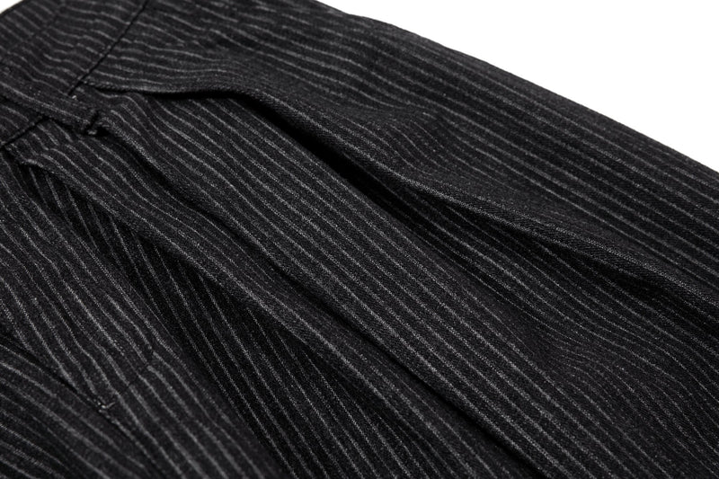 Close-up of pleated black pinstripe trousers from the hip area