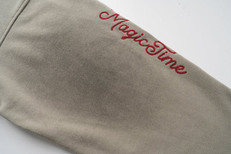 Red embroidered script on the sleeve of a taupe hoodie