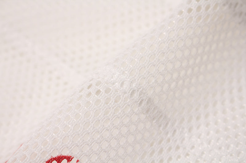 Close-up of white oversized mesh jersey fabric with a red flame sigil detail on the hem