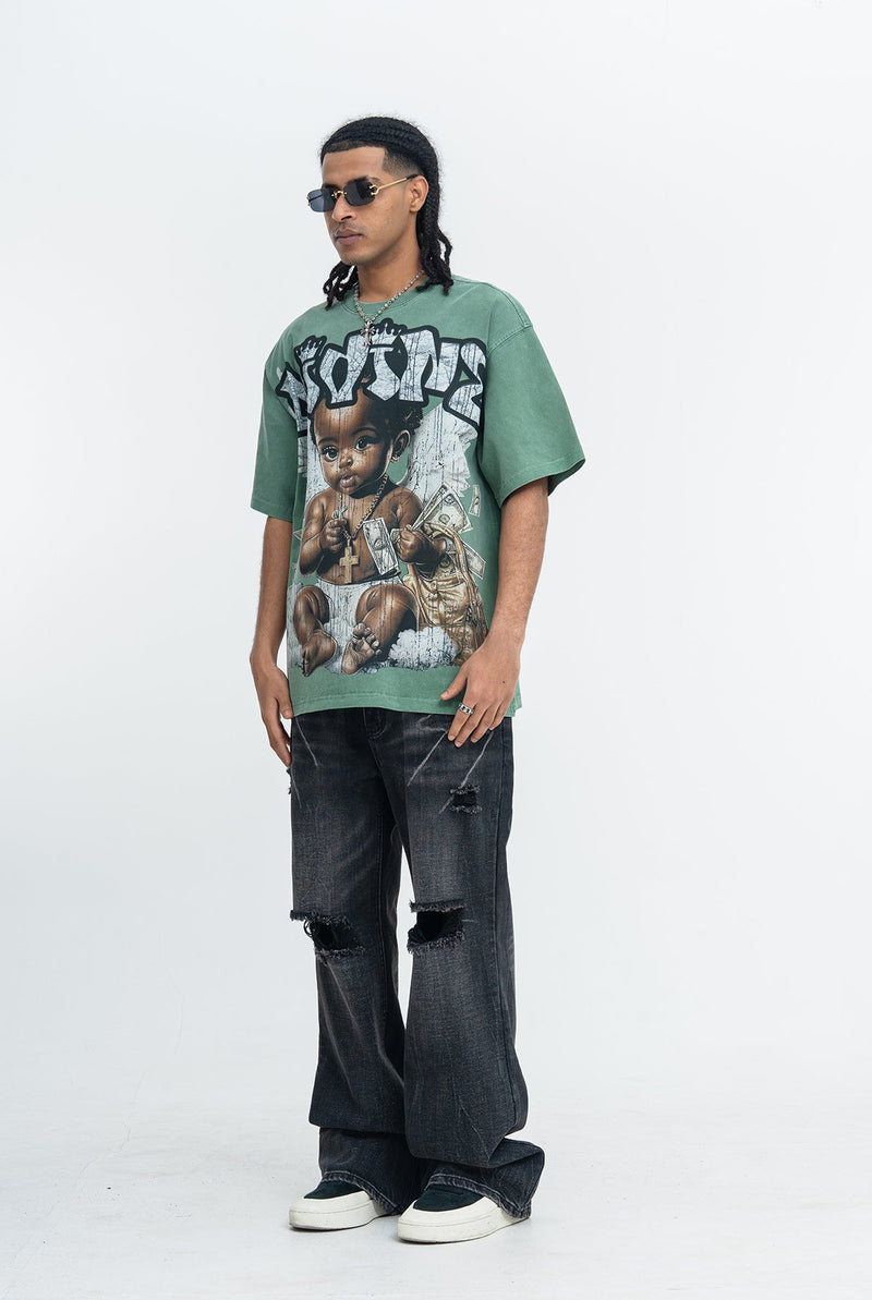 Green vintage wash graphic T-shirt with baby and money print, styled with distressed black jeans and sunglasses
