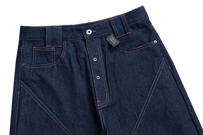 Front waist view of dark indigo denim jeans with curved seams, button fly, and topstitched pockets