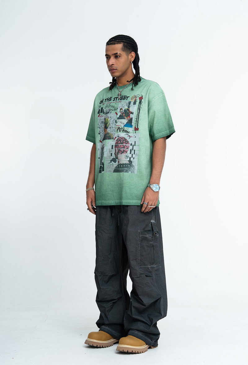 Model wearing a vintage wash green graphic tee with collage print, loose black cargo pants, and tan clogs on a white background