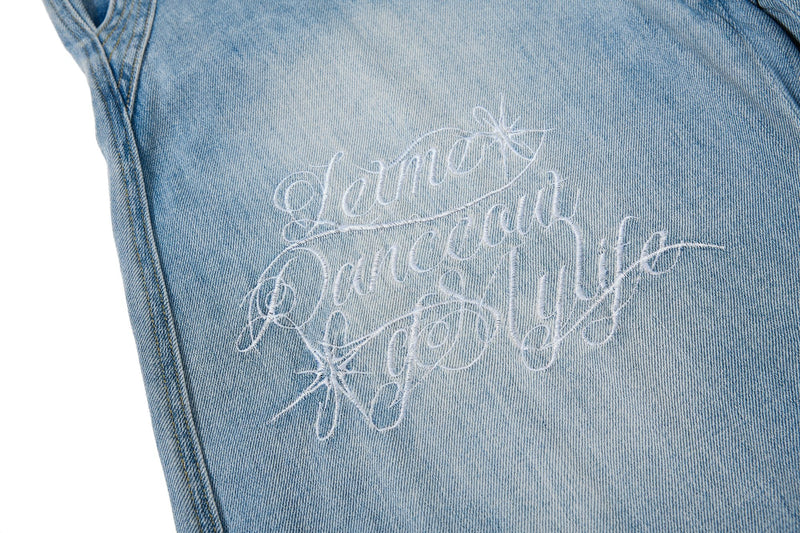 Close-up of embroidered script graphic on light wash denim leg