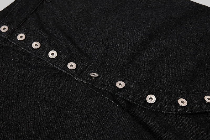 Close-up of the asymmetrical front button placket on black denim shorts