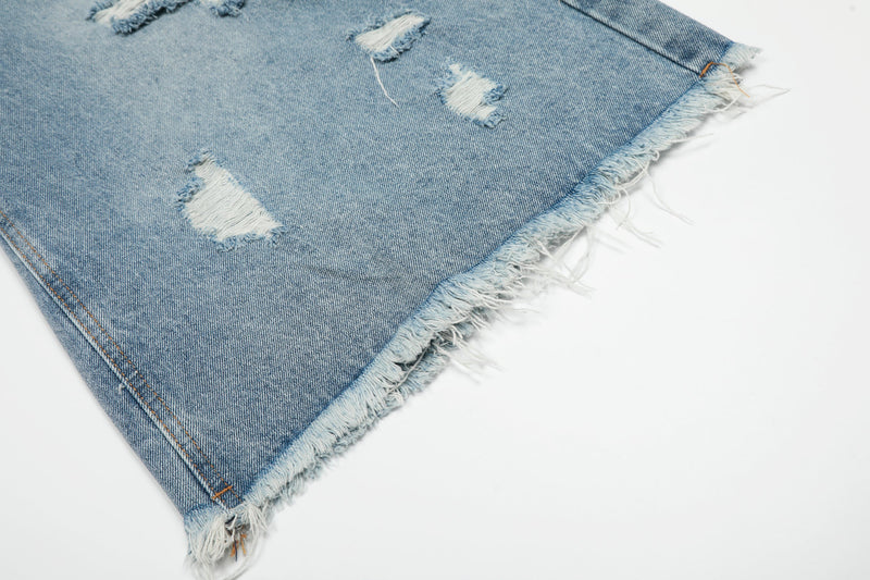 Close-up of frayed hem on light blue denim shorts with distressed holes