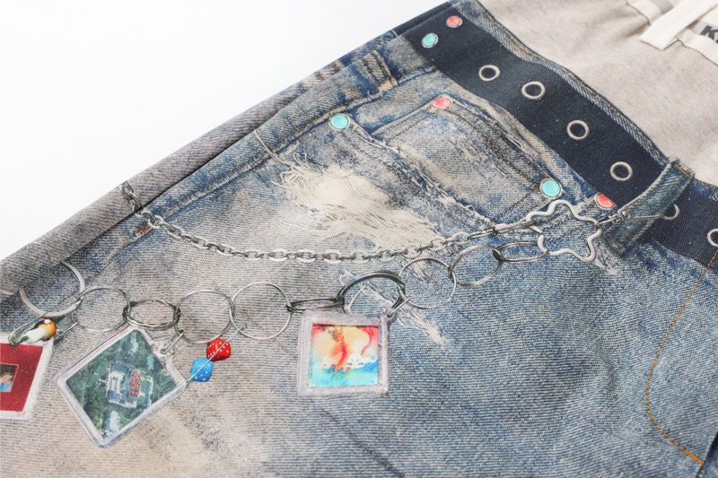 Upper front of distressed jeans with chain charm detail and printed belt graphic