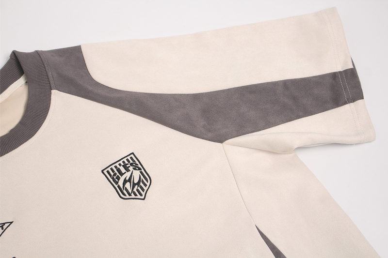 Cream and charcoal suede-panel tee with ribbed collar and bold sport-inspired chest logo