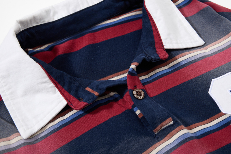 Close-up of white collar and button placket on navy, red, and cream striped rugby shirt
