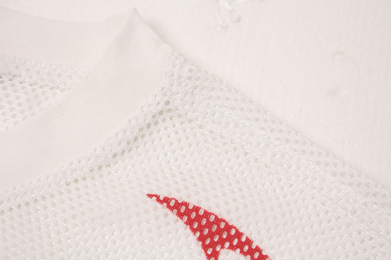 Close-up of white mesh athletic jersey fabric with red flame sigil detail and breathable perforated texture