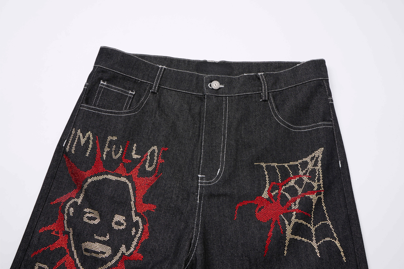 Front waist close-up of black denim jeans with rhinestone graffiti designs and white contrast stitching