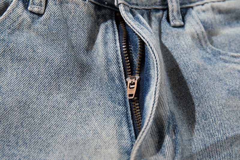 Close-up of the front zipper fly and waistband on light wash denim jeans