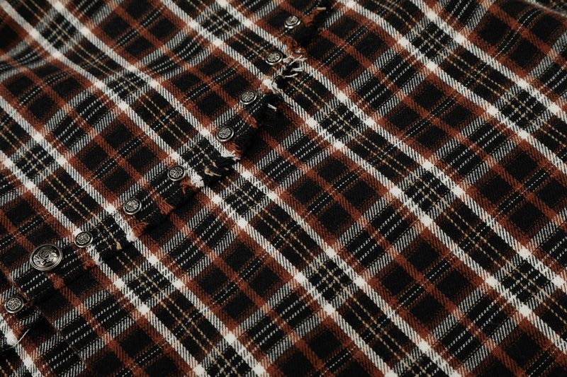 Close-up of distressed plaid shirt fabric with frayed seams and silver snap buttons in black, rust, and white plaid