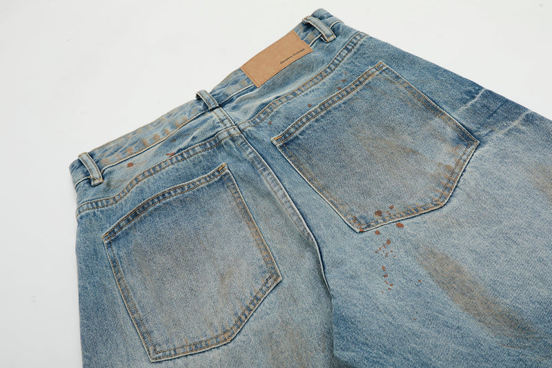 Close-up of back yoke and pockets on faded distressed blue jeans with rust-colored splatter marks