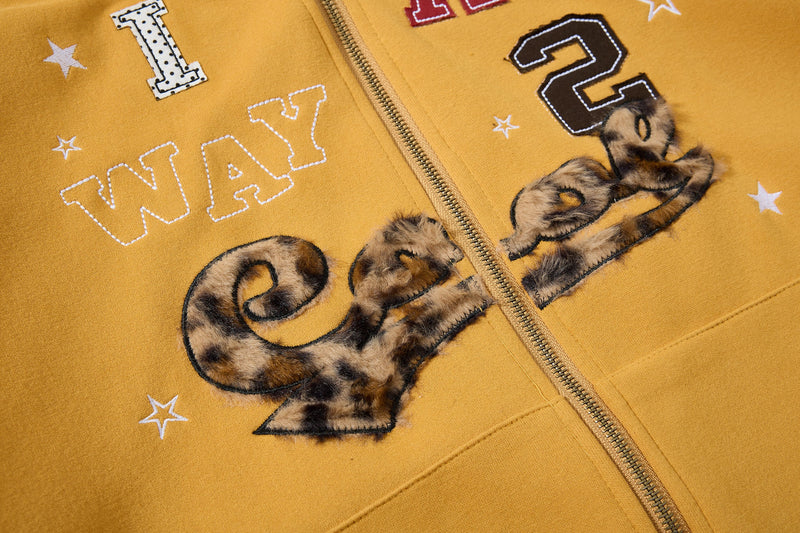Close-up of mustard yellow hoodie front graphic with leopard-print lettering and stars
