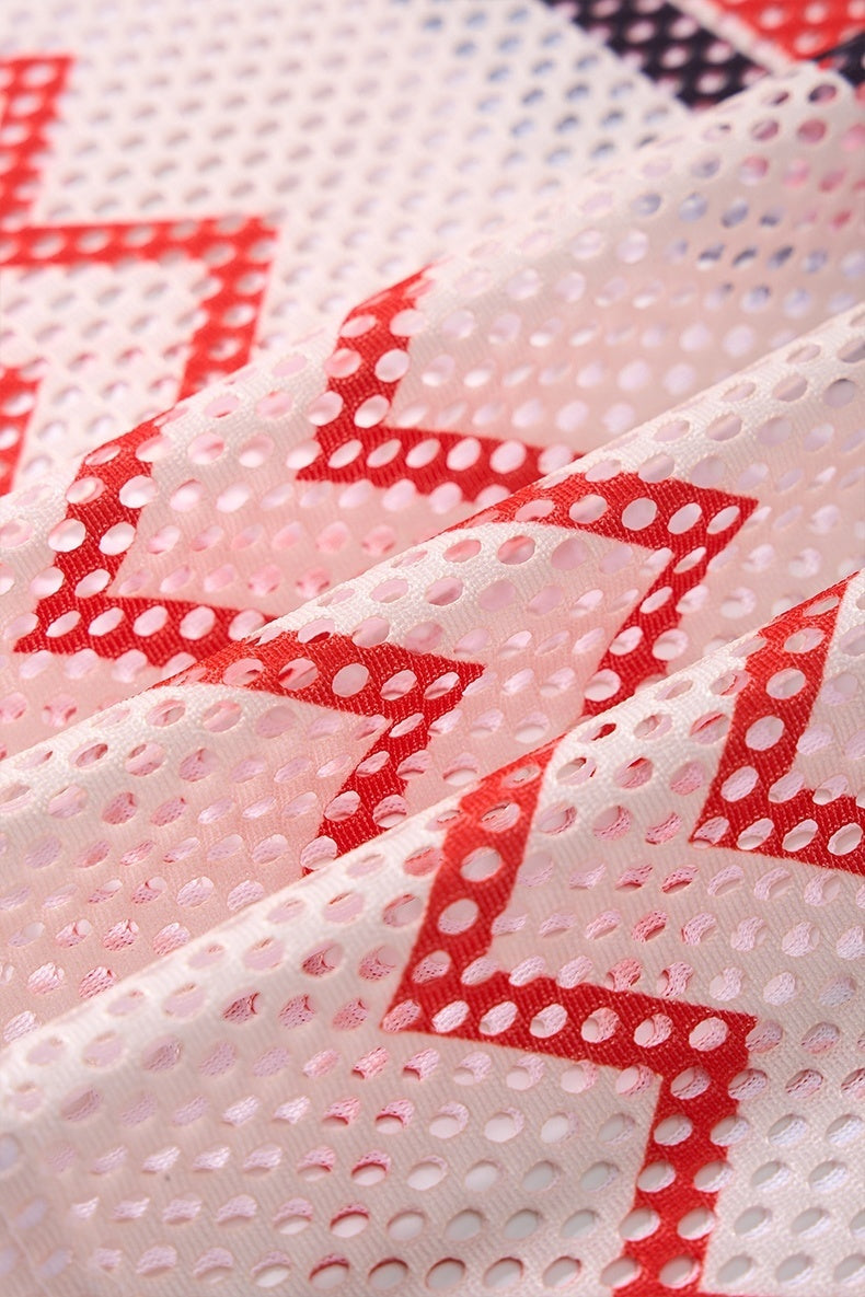 Close-up of white mesh jersey fabric with red geometric star pattern and perforated texture