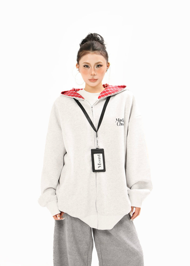 Model wearing a light gray zip-up hoodie with red plaid lining, logo print, and hanging tag