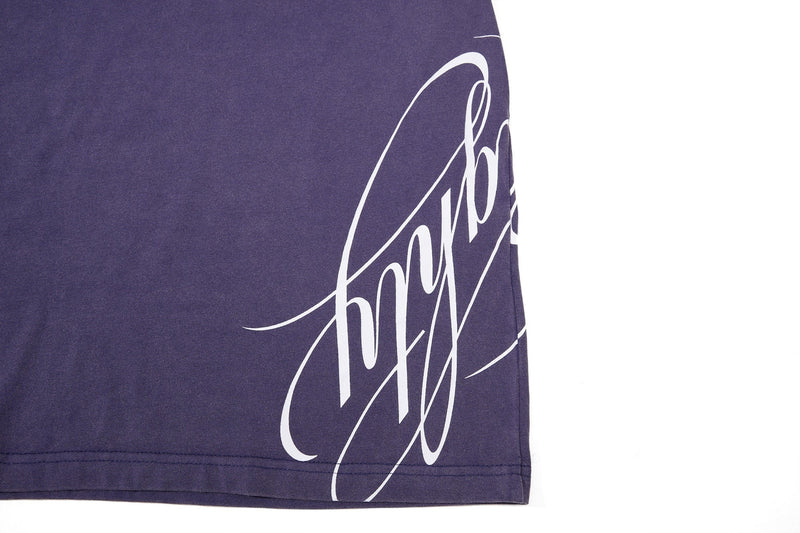 Close-up of a washed purple streetwear tee with large white crest-style graphic print on the hem