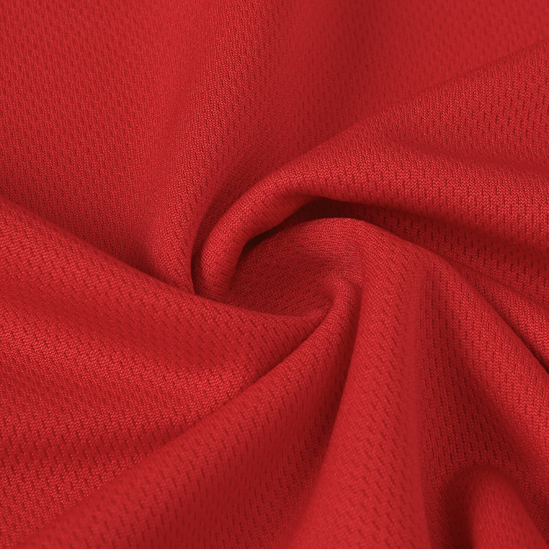 Close-up of red textured football jersey fabric with a soft folded swirl, sporty streetwear material visible