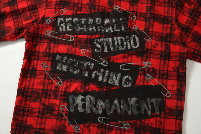 Front chest view of red plaid cropped shirt showing safety pin graphics and distressed text print