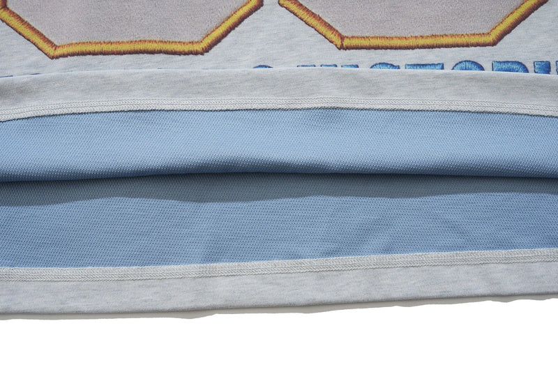 Close-up of a light blue varsity graphic tee with layered hem and stitched fabric details
