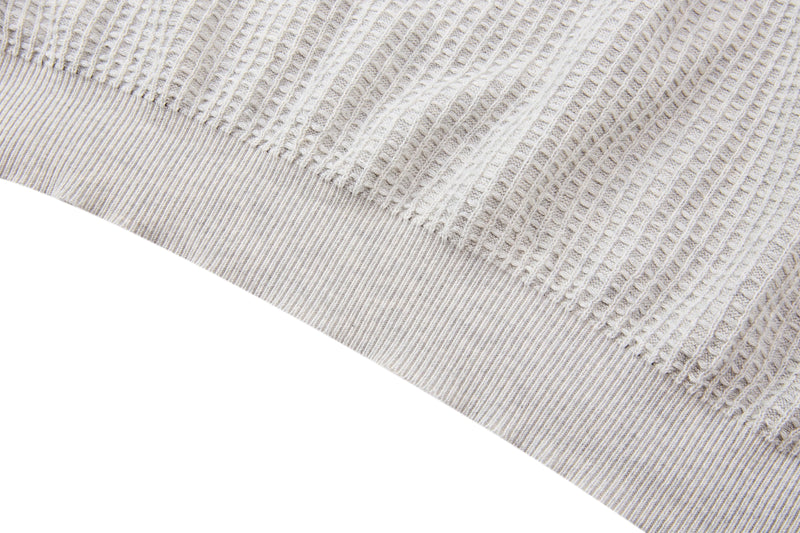 Close-up of a cream waffle knit short-sleeve sweater with ribbed hem and textured cotton blend fabric