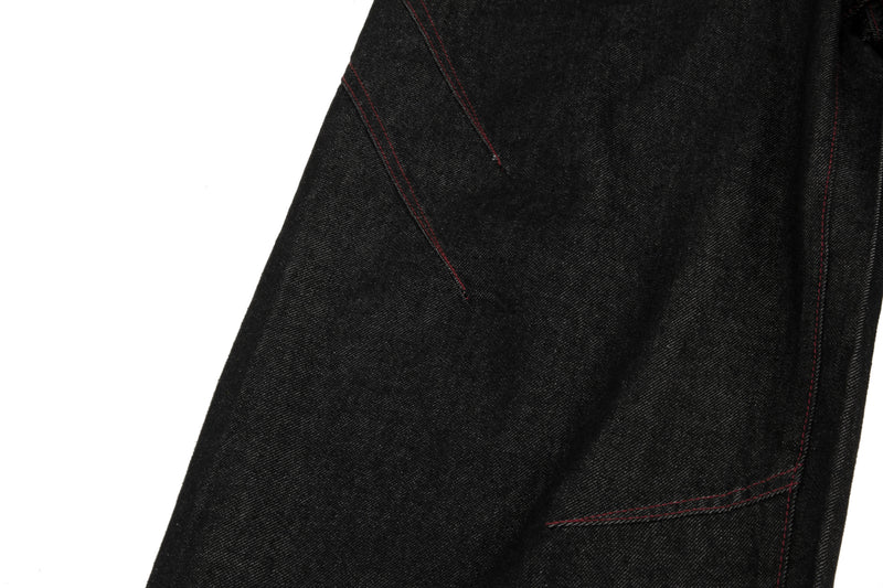 Close-up of black denim leg seam with contrast red stitching and wide hem