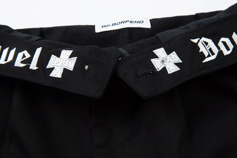 Close-up of waistband label and white embroidered cross motifs on black pants