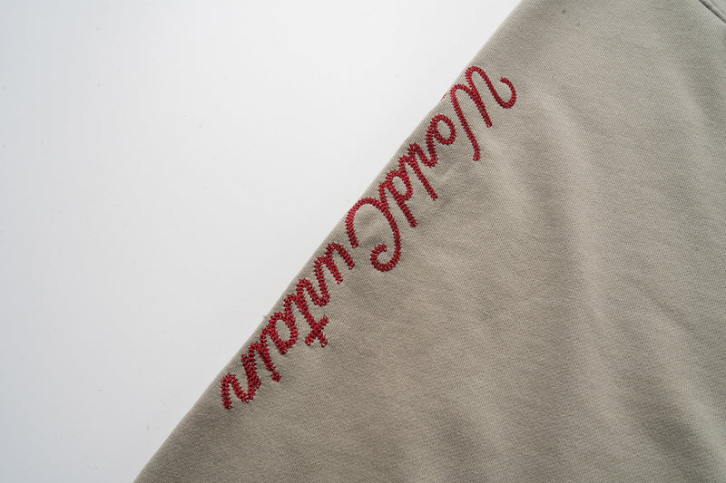 Red embroidered sleeve text on taupe hoodie, angled view