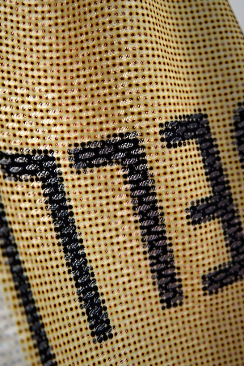 Close-up of beige vintage mesh jersey with black patchwork lettering and perforated streetwear texture
