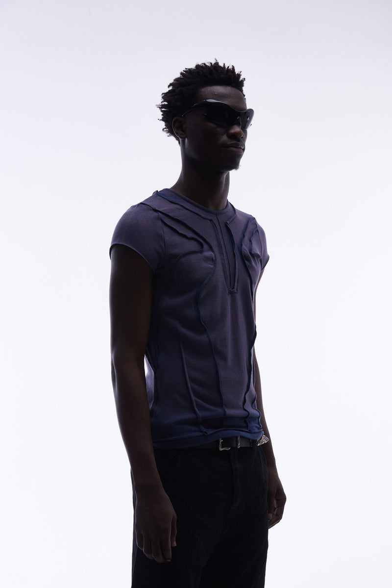 Model wearing a navy sculpted cotton tee with raw seams and panel detailing, styled with black sunglasses on a white background
