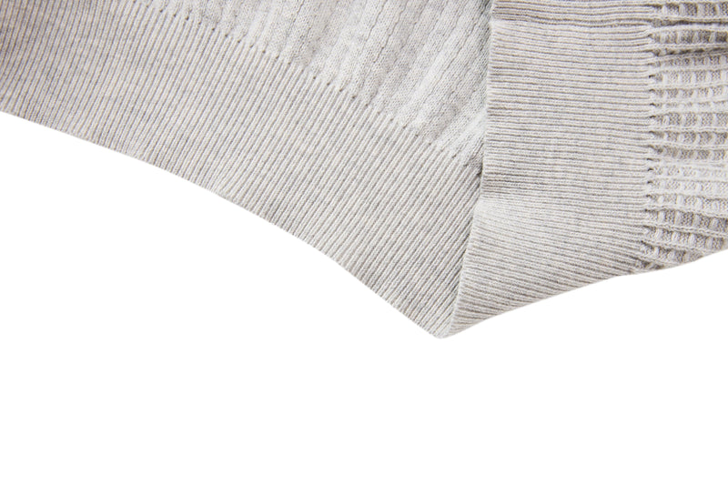 Close-up of a beige waffle knit short-sleeve sweater sleeve with ribbed cuff and textured cotton blend fabric