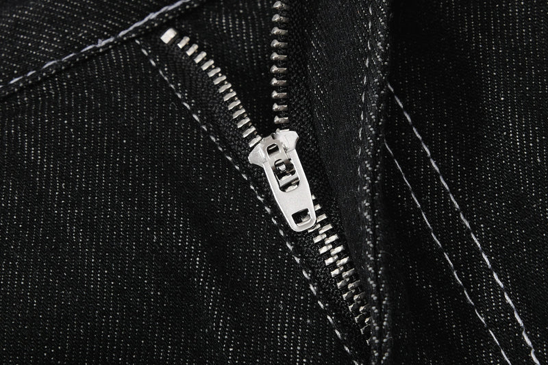 Close-up of silver zipper on black denim pants with white topstitching