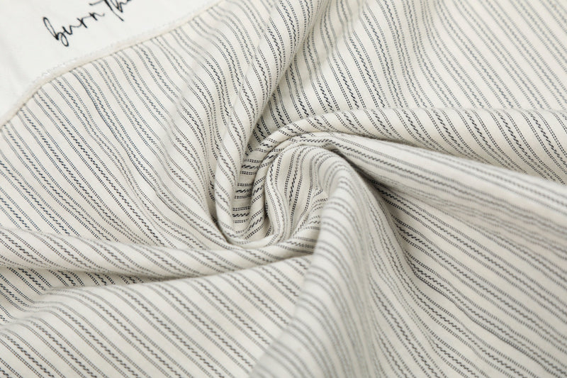 Cream pinstripe button-up shirt with black stitched graphic details and soft folded fabric texture