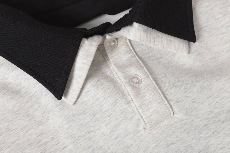 Close-up of light gray polo front with clear buttons and black layered collar detail